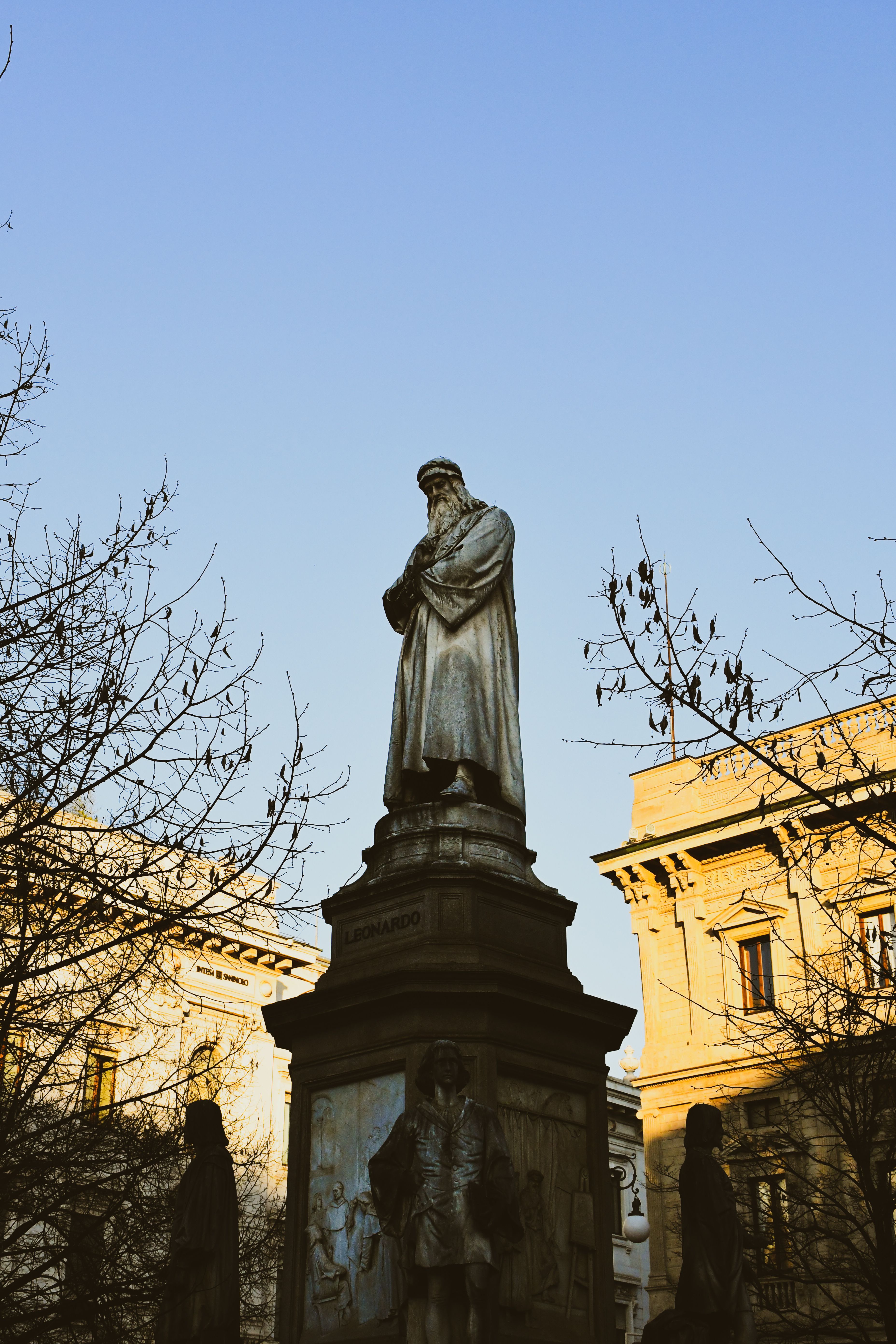A historic statue in a European square during sunrise with architectural buildings.