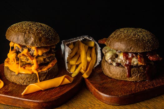 Close-up of two gourmet cheeseburgers with fries on wooden boards. Delicious fast food concept.