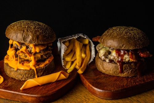 Free Close-up of two gourmet cheeseburgers with fries on wooden boards. Delicious fast food concept. Stock Photo