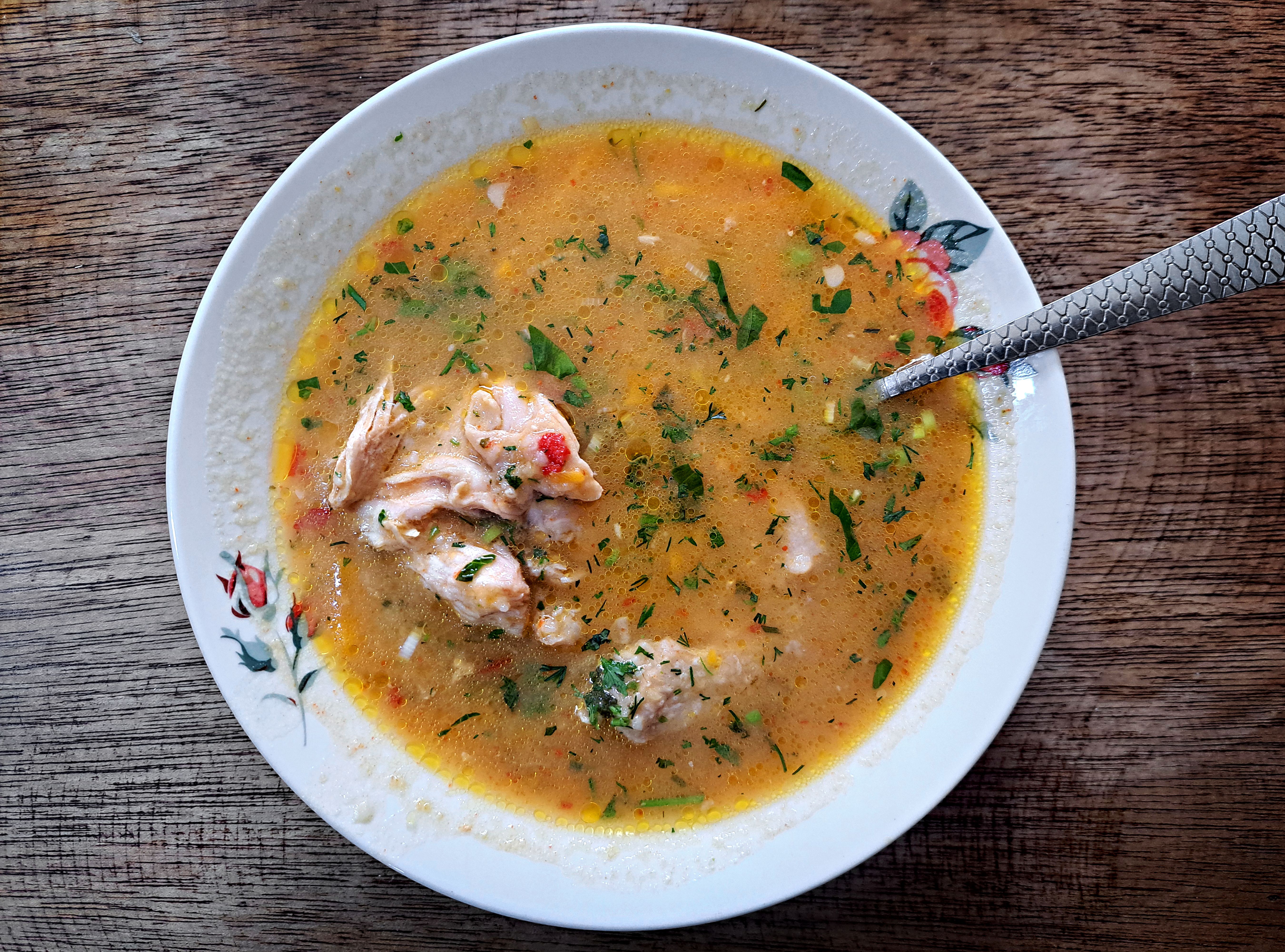 A top view of traditional Ecuadorian fish soup in a floral bowl with herbs on a wooden table.