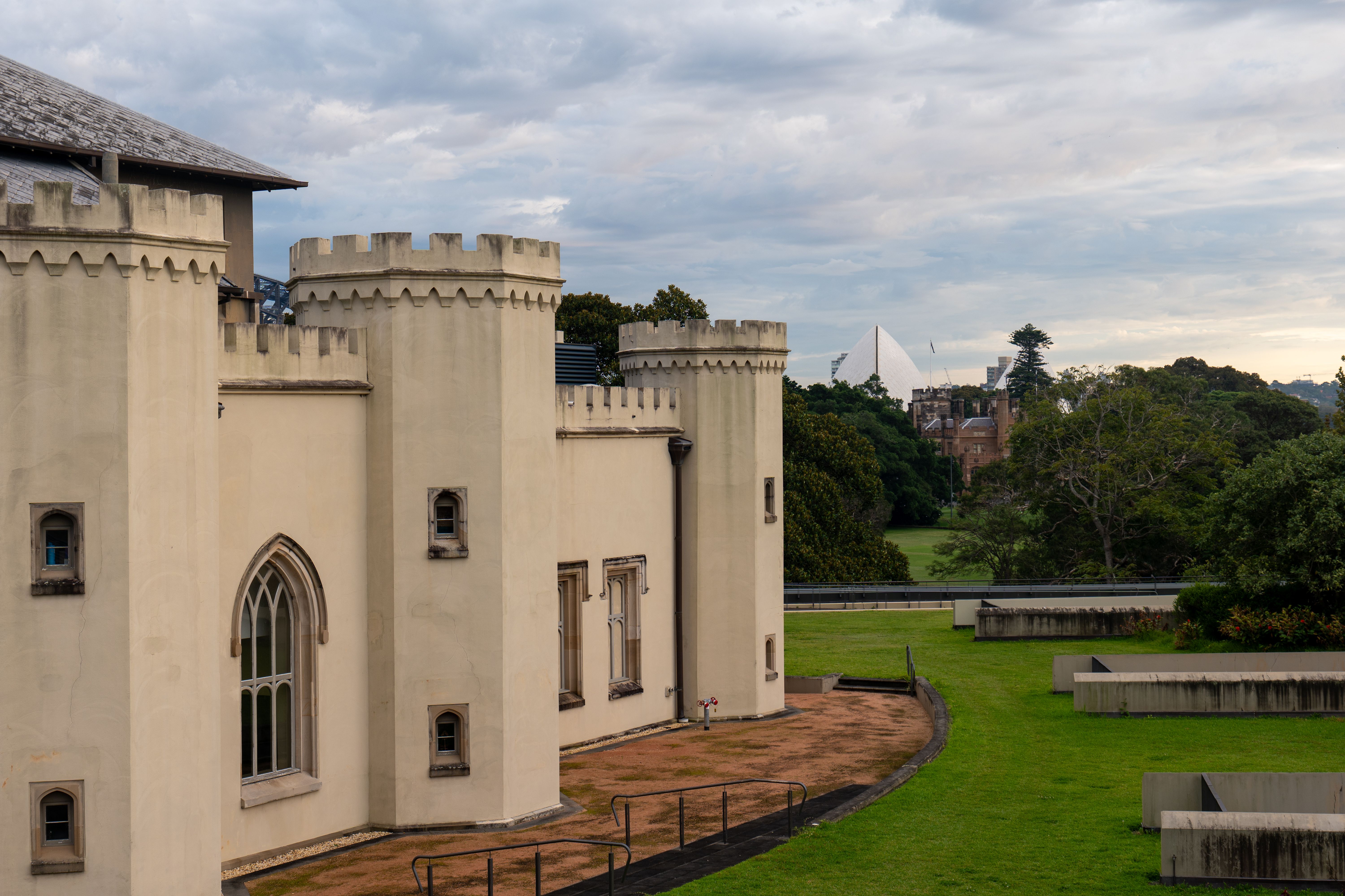 A historic castle building with Sydney's skyline in the background on a cloudy day.