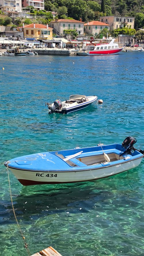 Free Two boats anchored in turquoise waters near a coastal town on a sunny day. Stock Photo