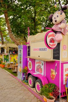 Charming pink food truck in park serving fondue waffles, adorned with plush toys.