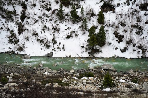 Free A serene river flows through a snowy mountainous landscape with evergreen trees. Stock Photo