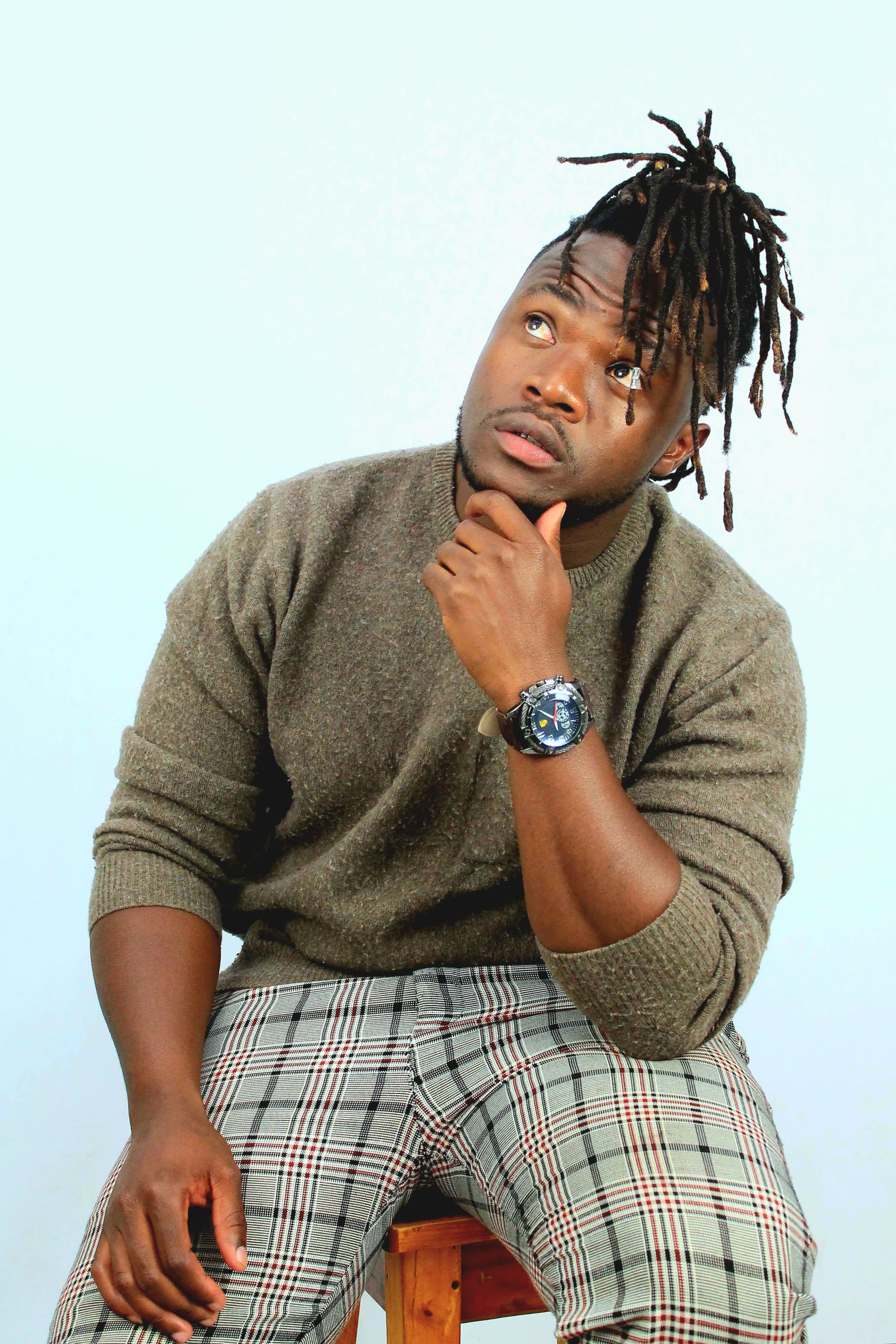 A fashionable man with dreadlocks sits thoughtfully, embodying modern style.