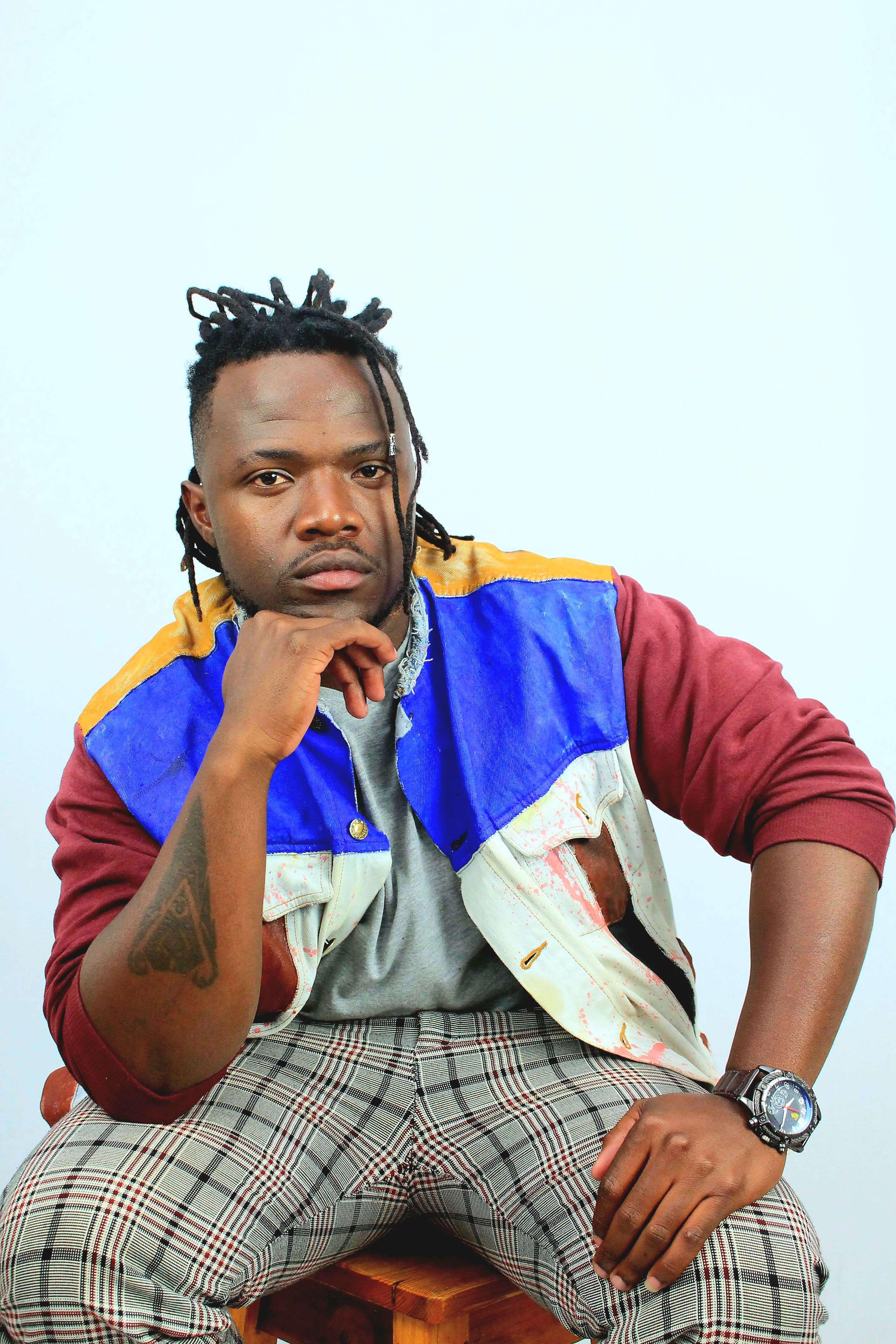 A striking portrait of a fashionable man in colorful attire sitting thoughtfully, showcasing unique style.