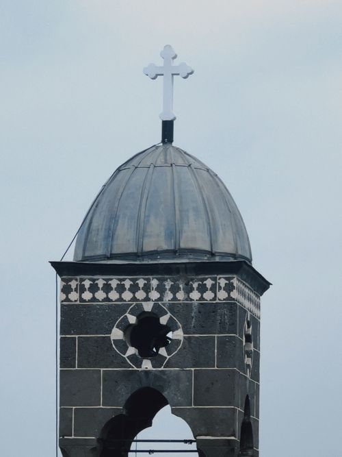 Free Close-up of a historic church tower with a cross, showcasing intricate stonework against a cloudy sky. Stock Photo