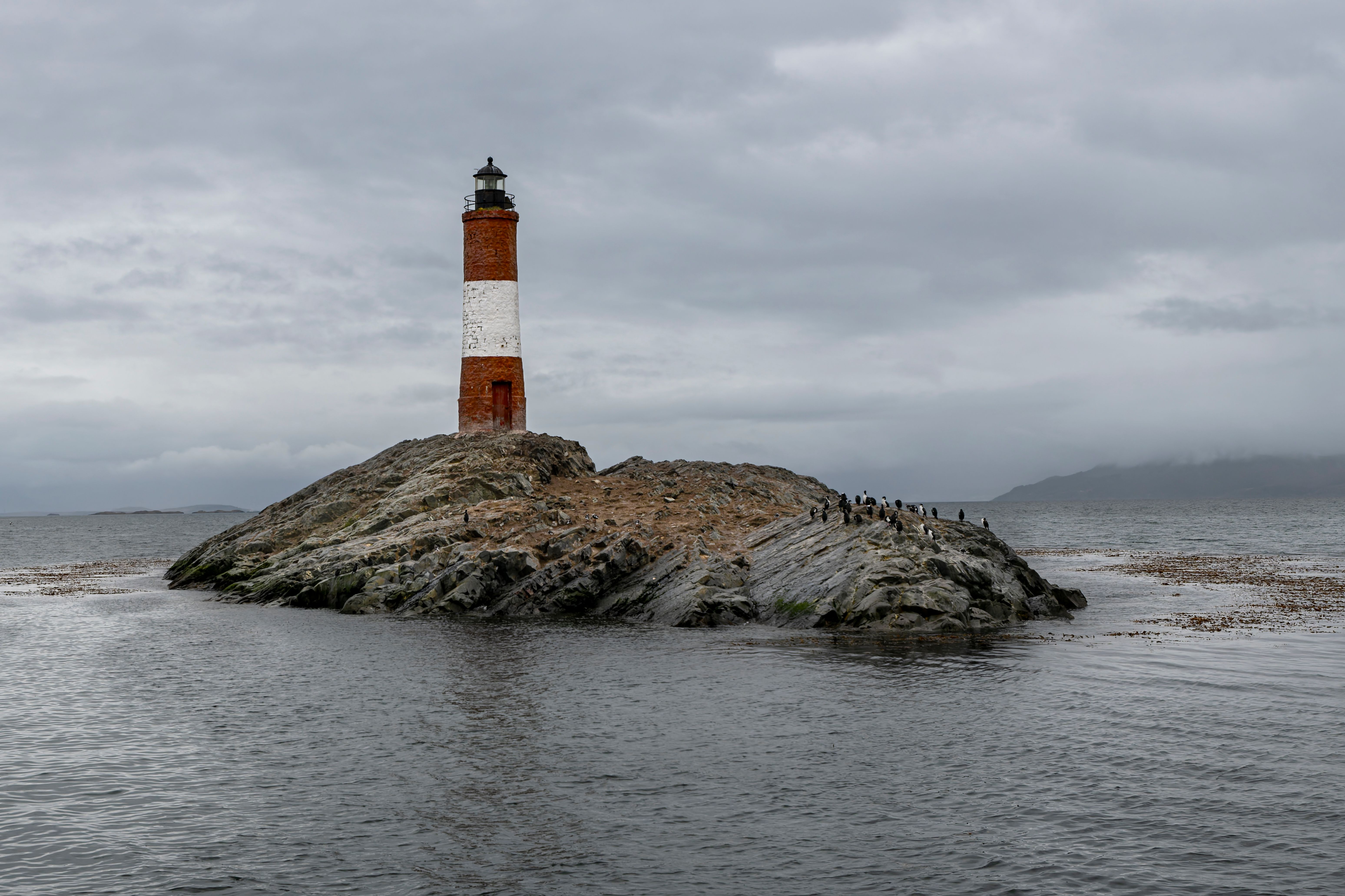 Majestic Les Eclaireurs Lighthouse Standing On Rocky Outcrop In Ushuaia, Argentina, Against A Cloudy Sky.