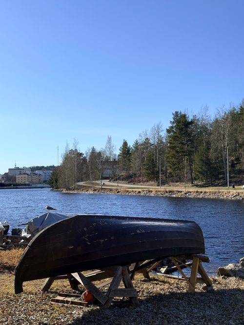 Free An overturned boat rests on a tranquil lakeside in Savonlinna, surrounded by spring greenery. Stock Photo