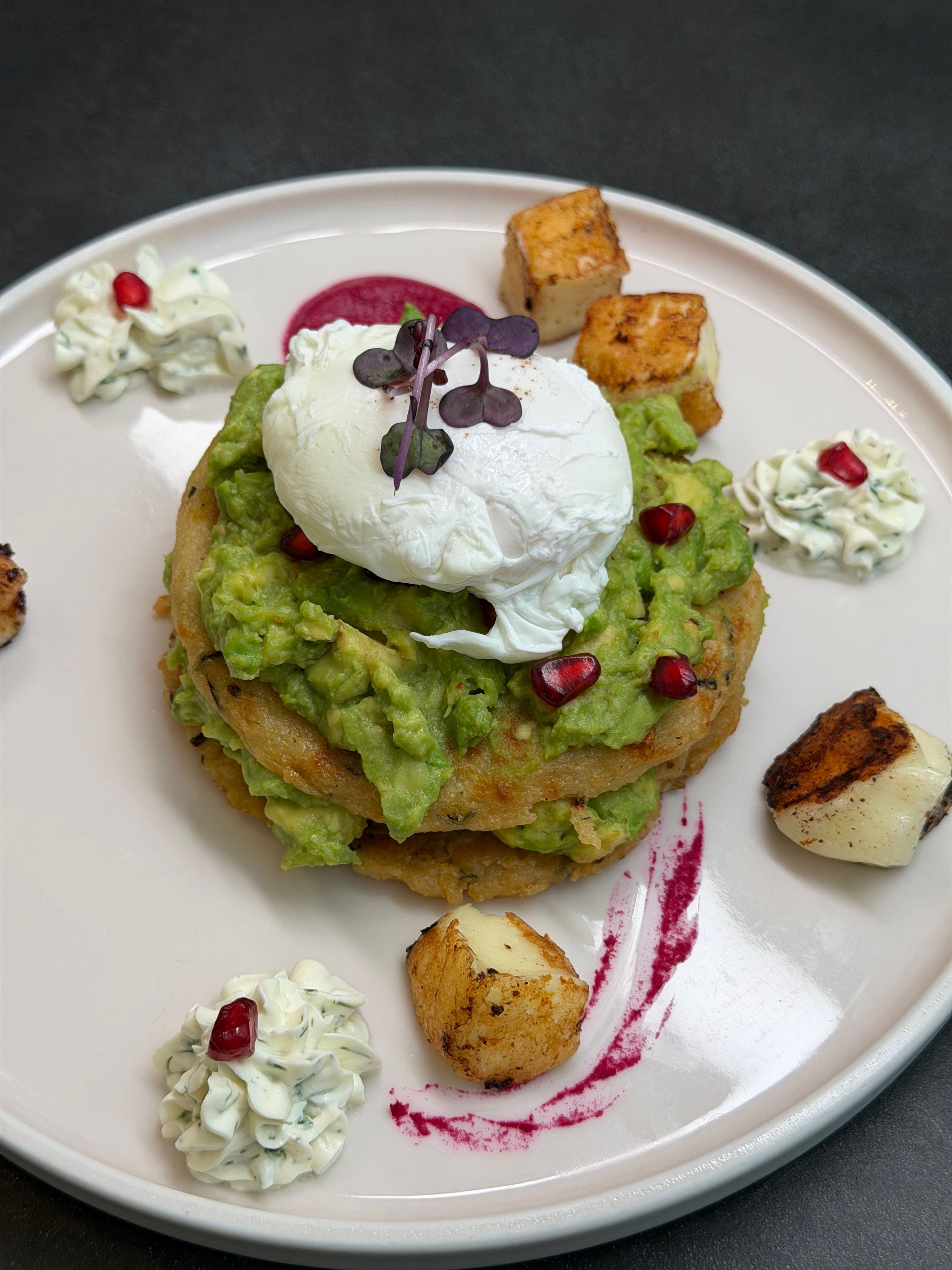 Delicious avocado toast with poached egg, garnished with pomegranate and potatoes.