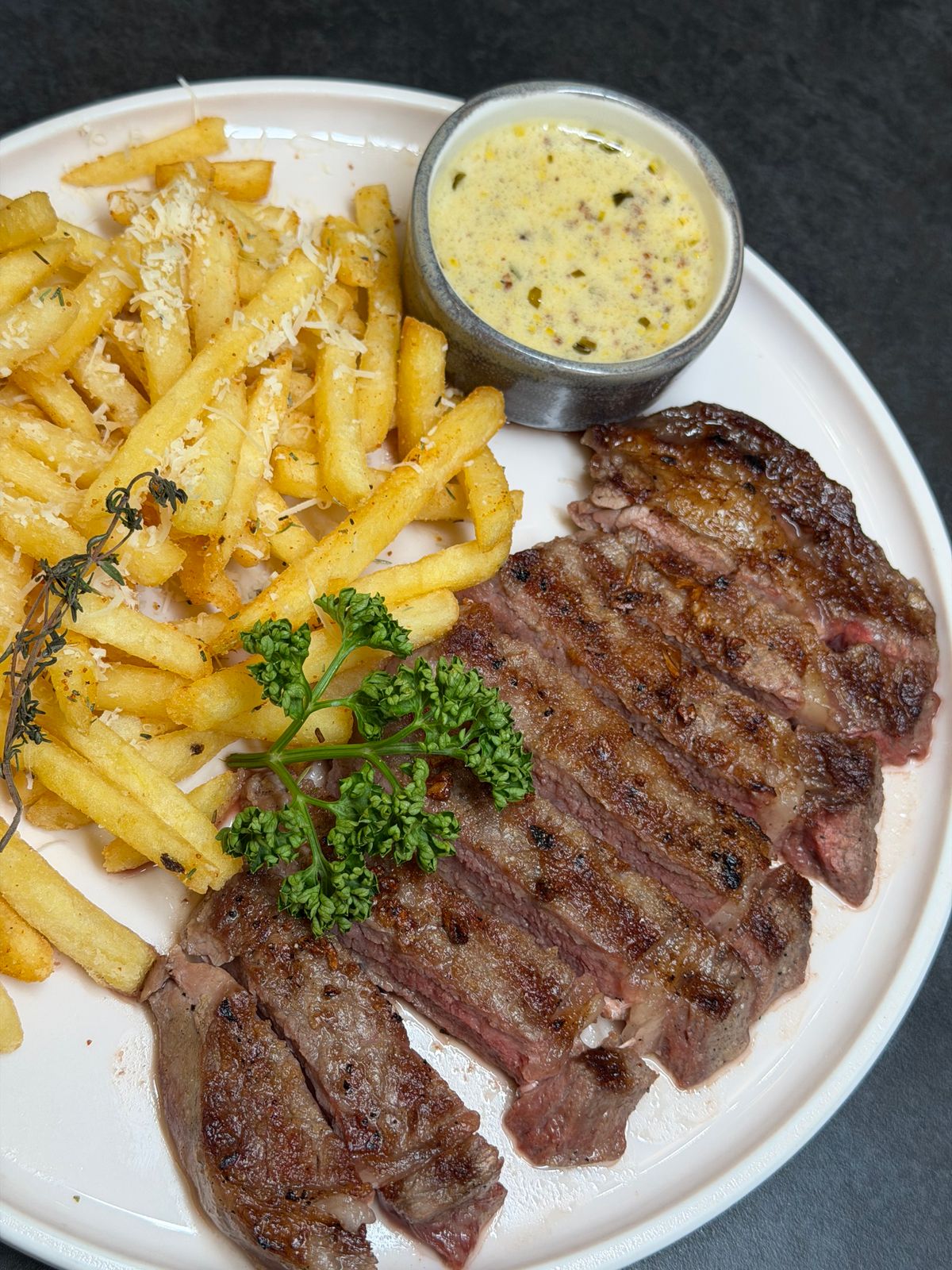 Grilled ribeye steak sliced across the grain with a mound of crispy shoestring fries and a ramekin of creamy mustard sauce
