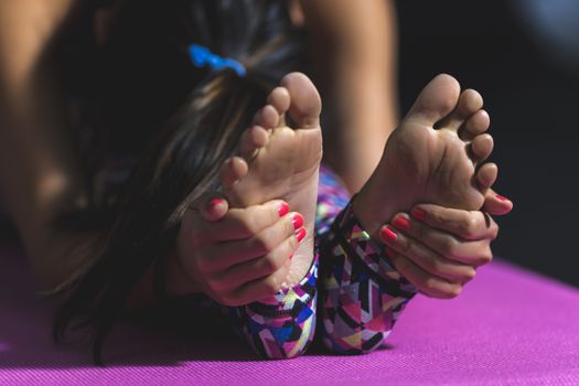 Close-up of woman performing yoga stretching exercise on a pink mat, focusing on feet.