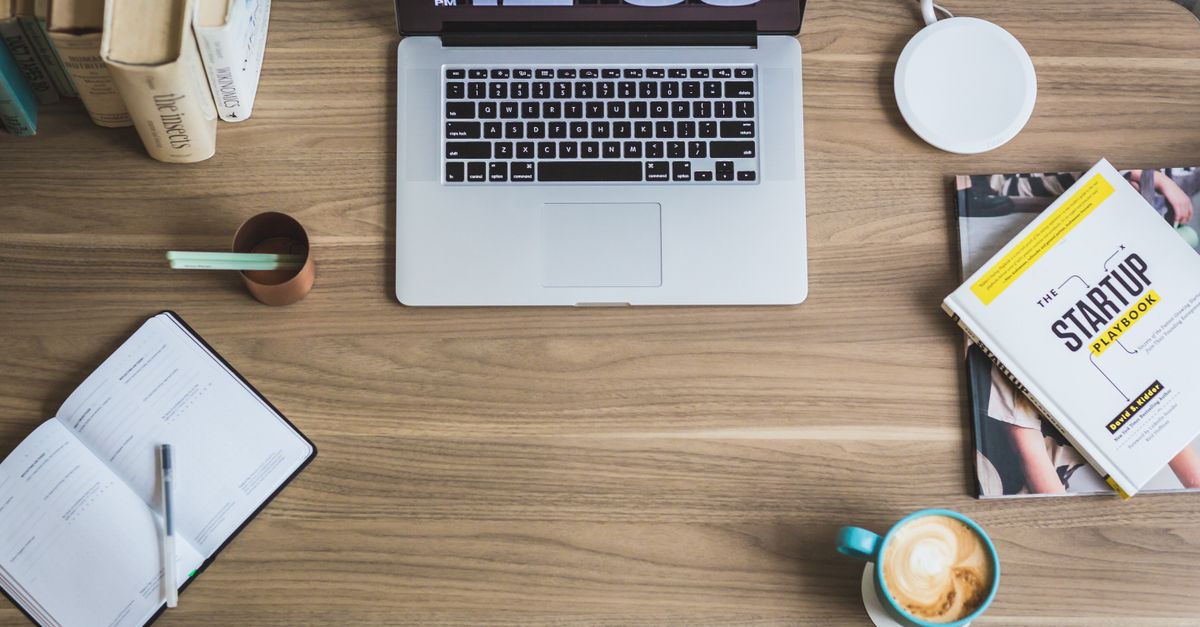 A stack of finance books with a coffee cup on a wooden desk