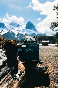 A vintage Instax camera with scenic Kananaskis mountains in the background.