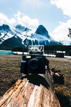 Capture of a camera with an Instax photo against Kananaskis mountain backdrop outdoors.