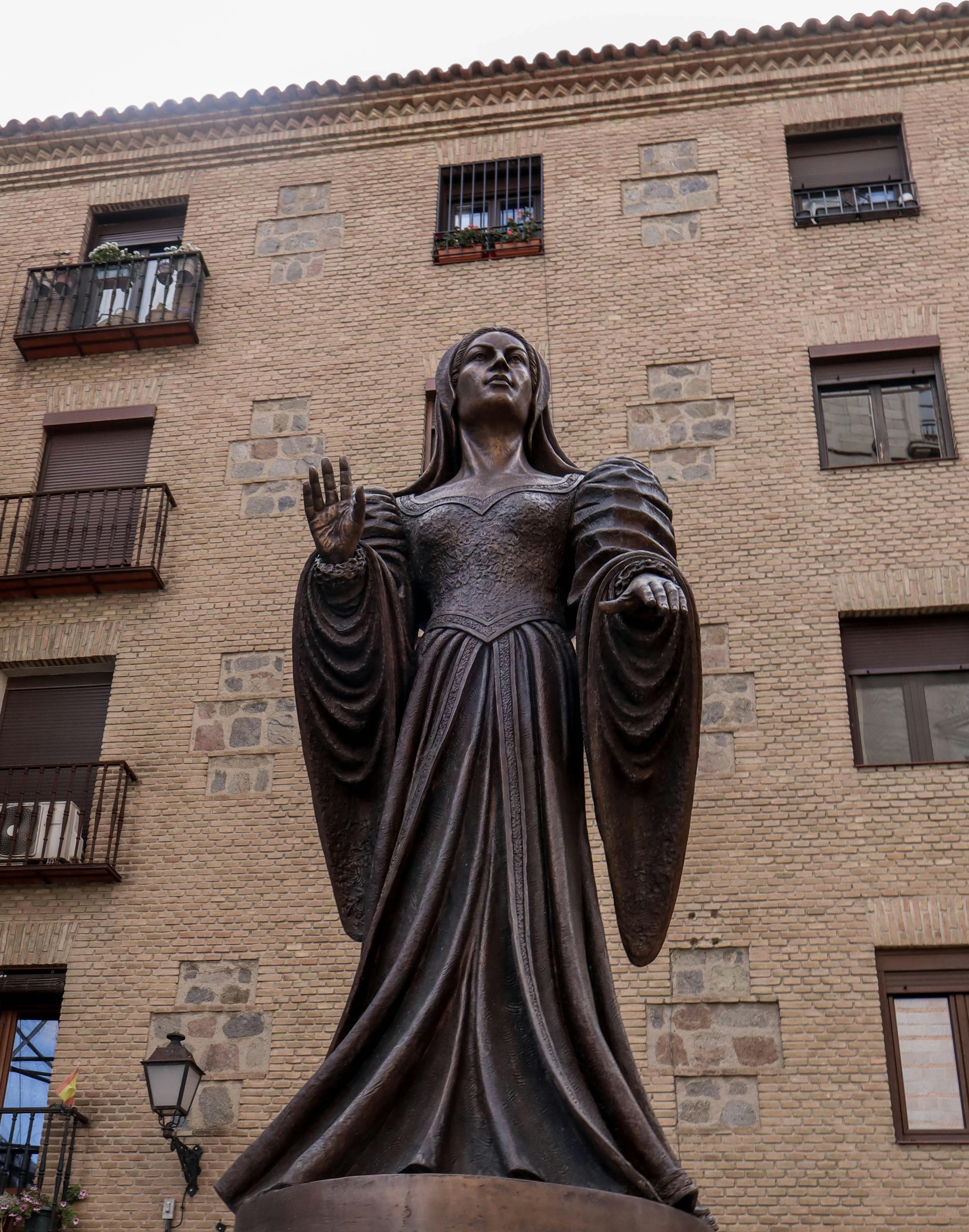 Bronze statue of a woman in front of a historic building in Toledo, Spain.