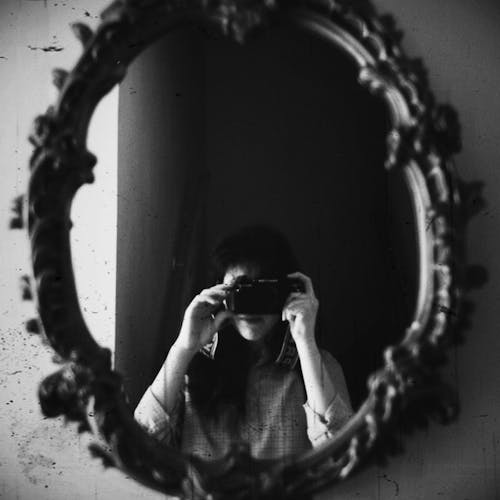 Grayscale Photo of Woman Taking Photo of an Antique Mirror