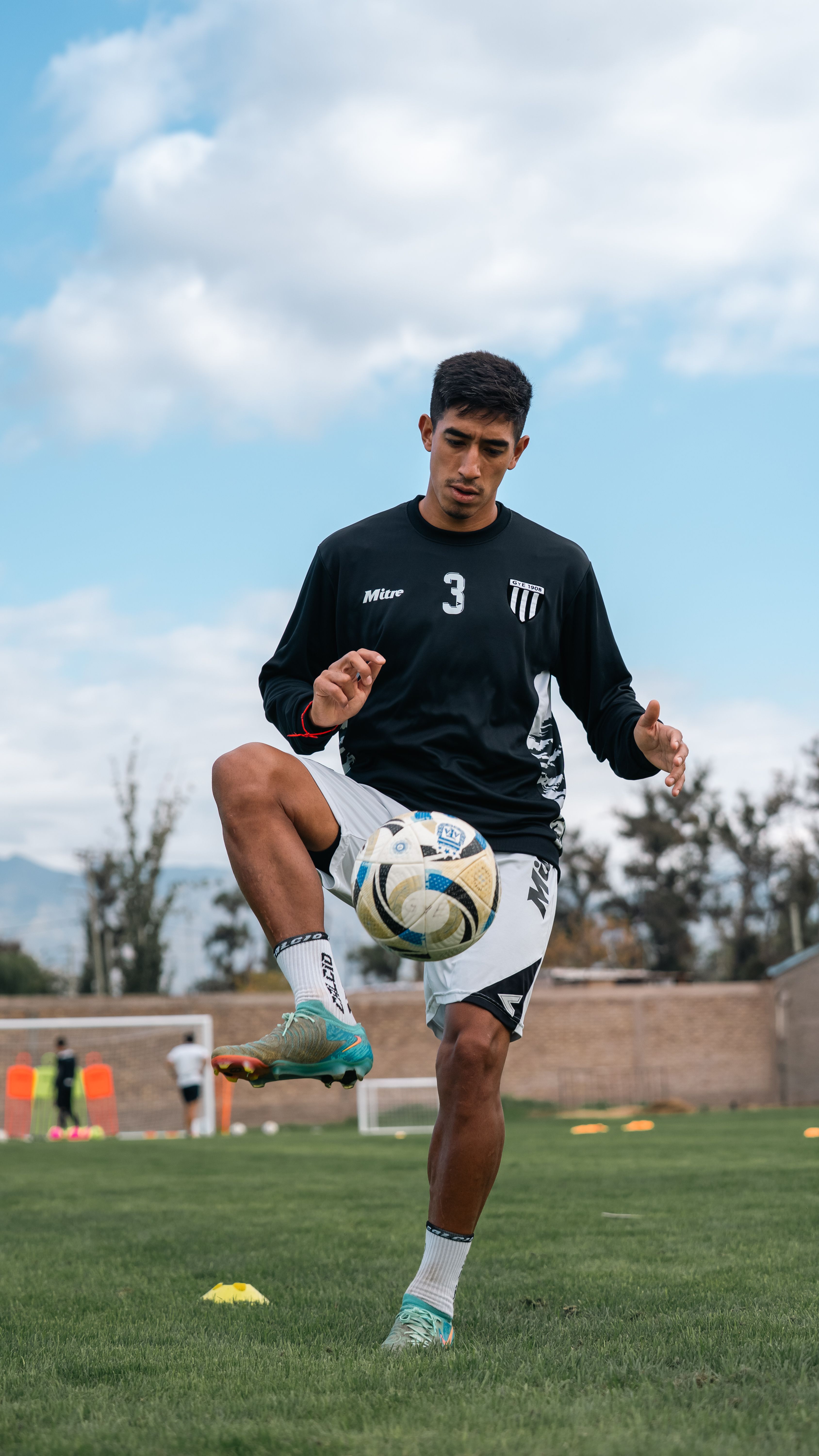 A young male soccer player practicing ball control on a grassy field outdoors.