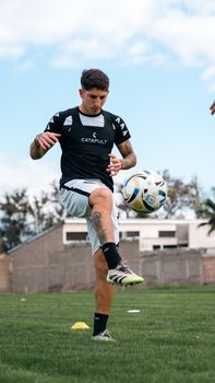 A young man practicing soccer on a grassy field wearing athletic gear, balancing a soccer ball.