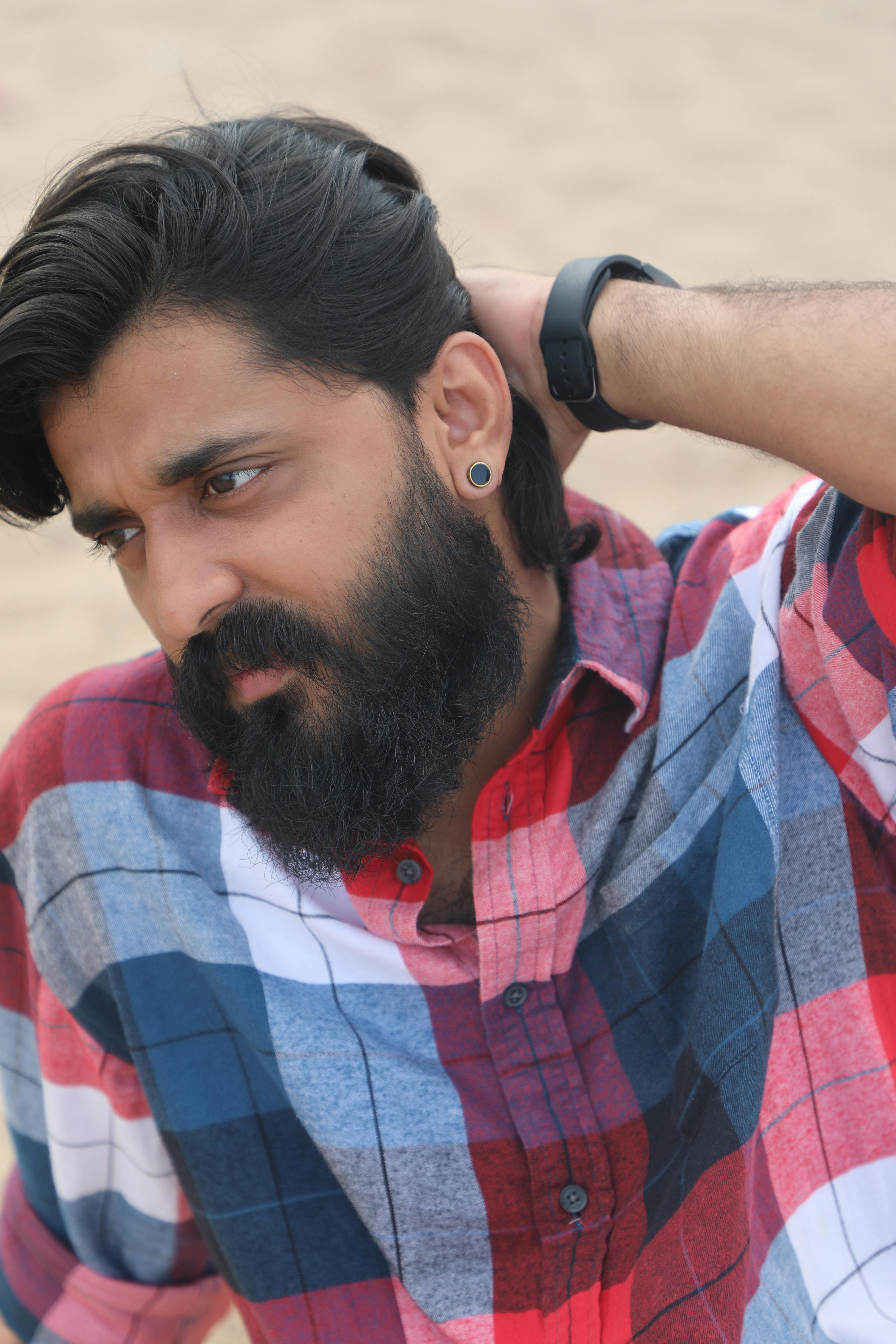 Bearded man in a plaid shirt poses thoughtfully outdoors, wearing a smartwatch.