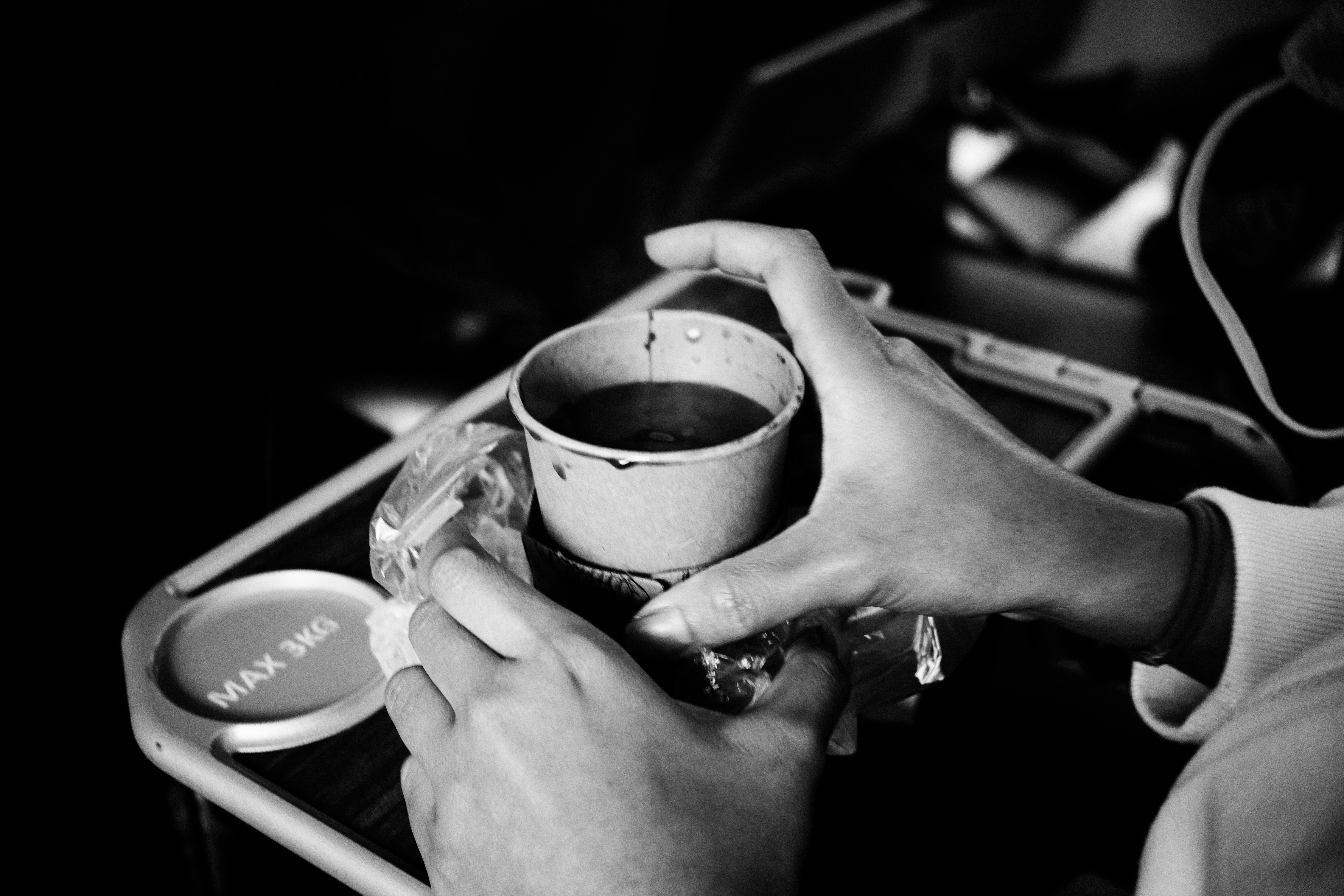 A grayscale capture of hands holding a drink cup on an airplane tray table.
