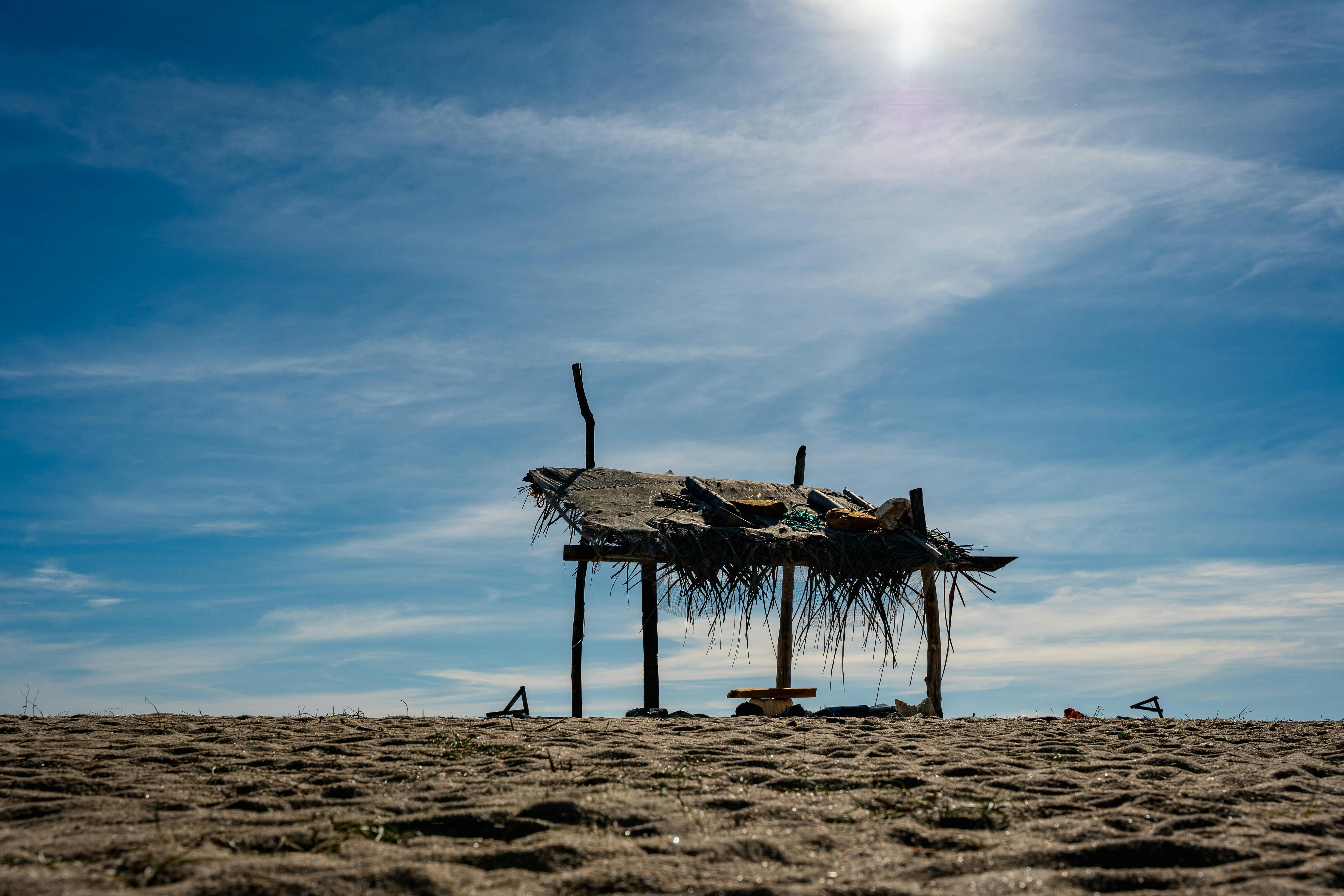 A rustic beach hut stands under a bright blue sky on a sandy beach in Batticaloa, Sri Lanka.