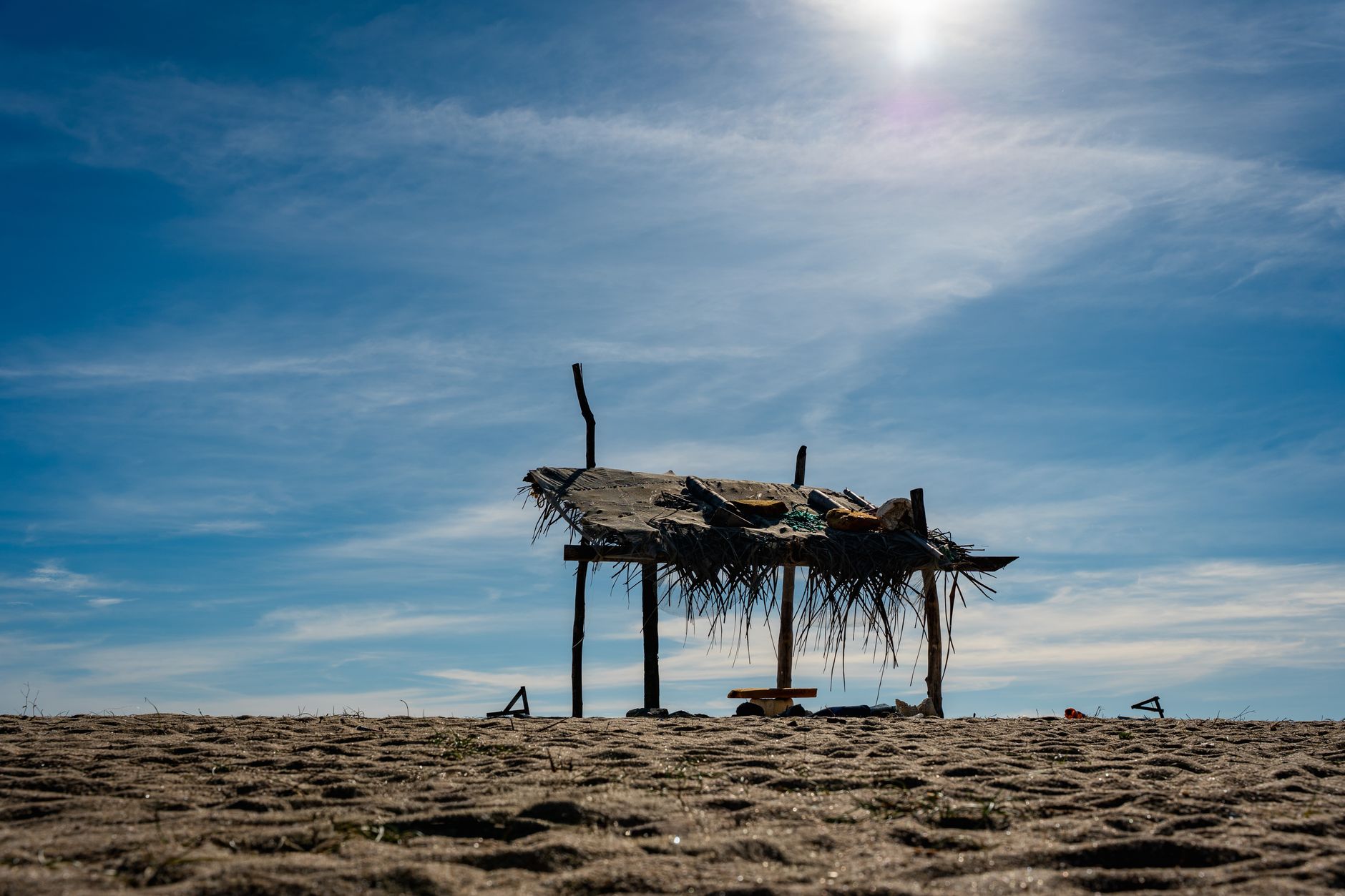 A rustic beach hut stands under a bright blue sky on a sandy beach in Batticaloa, Sri Lanka.