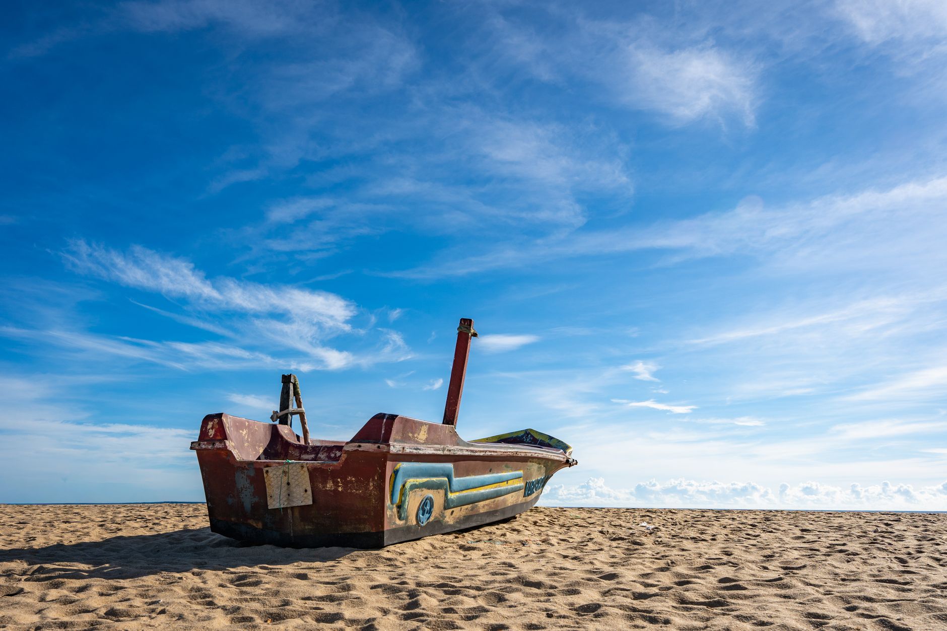 A vibrant boat rests on the sandy beach under a clear blue sky in Batticaloa, Sri Lanka.
