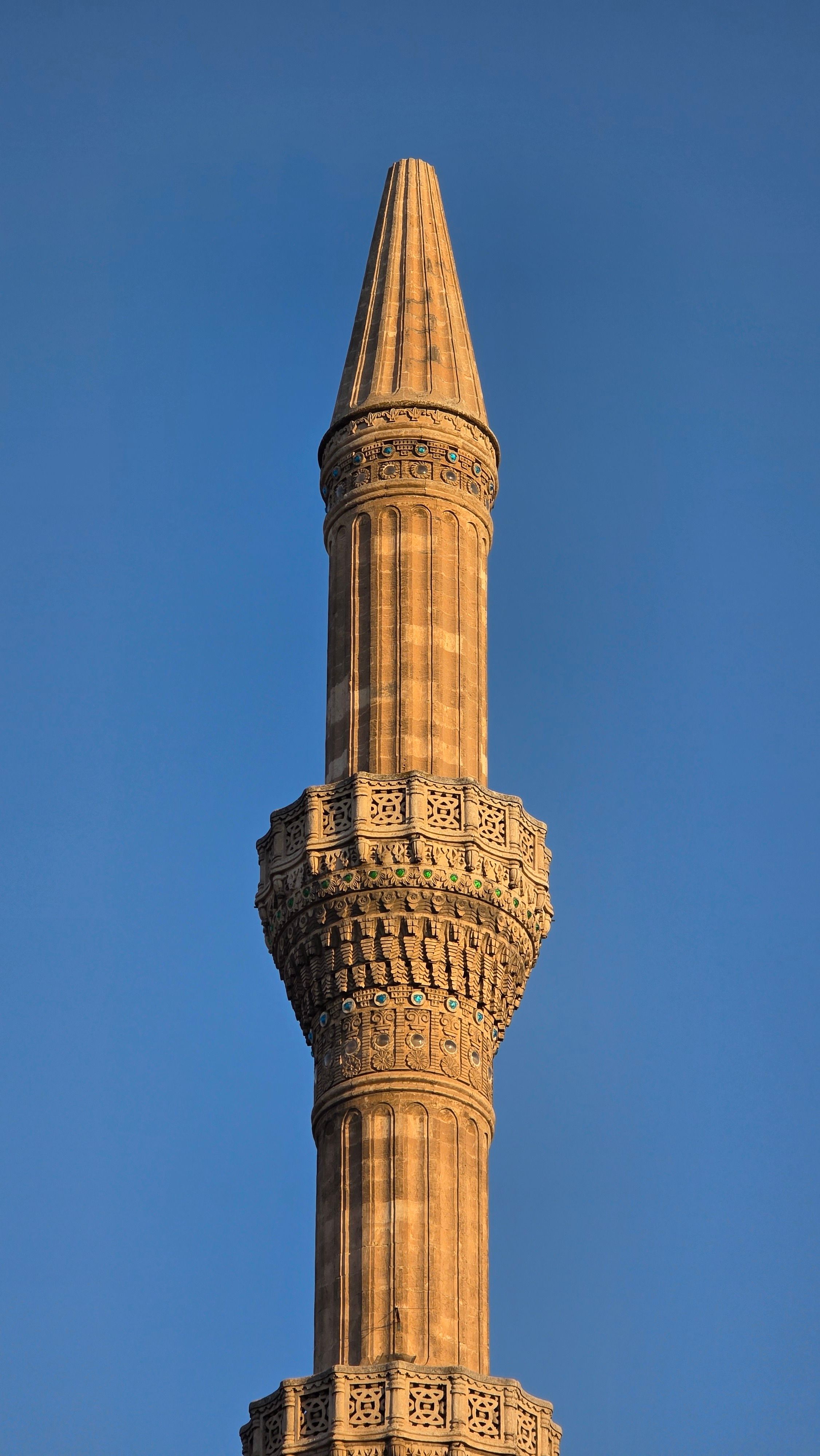 A close-up view of a detailed minaret against a clear blue sky, showcasing intricate stonework.