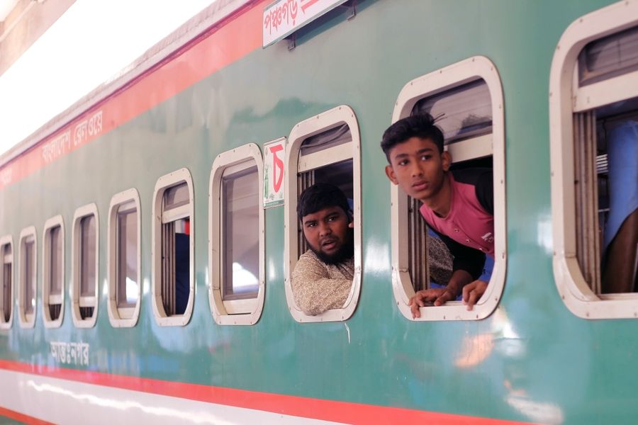 People looking out of train windows at a station in Bangladesh, showcasing local travel culture.