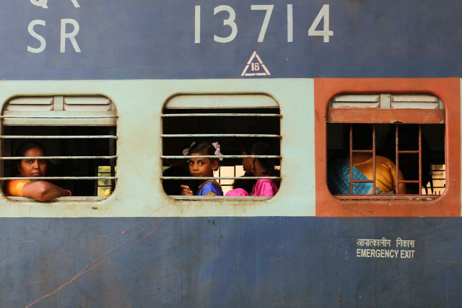 A candid view inside an Indian train with passengers looking outside through barred windows.