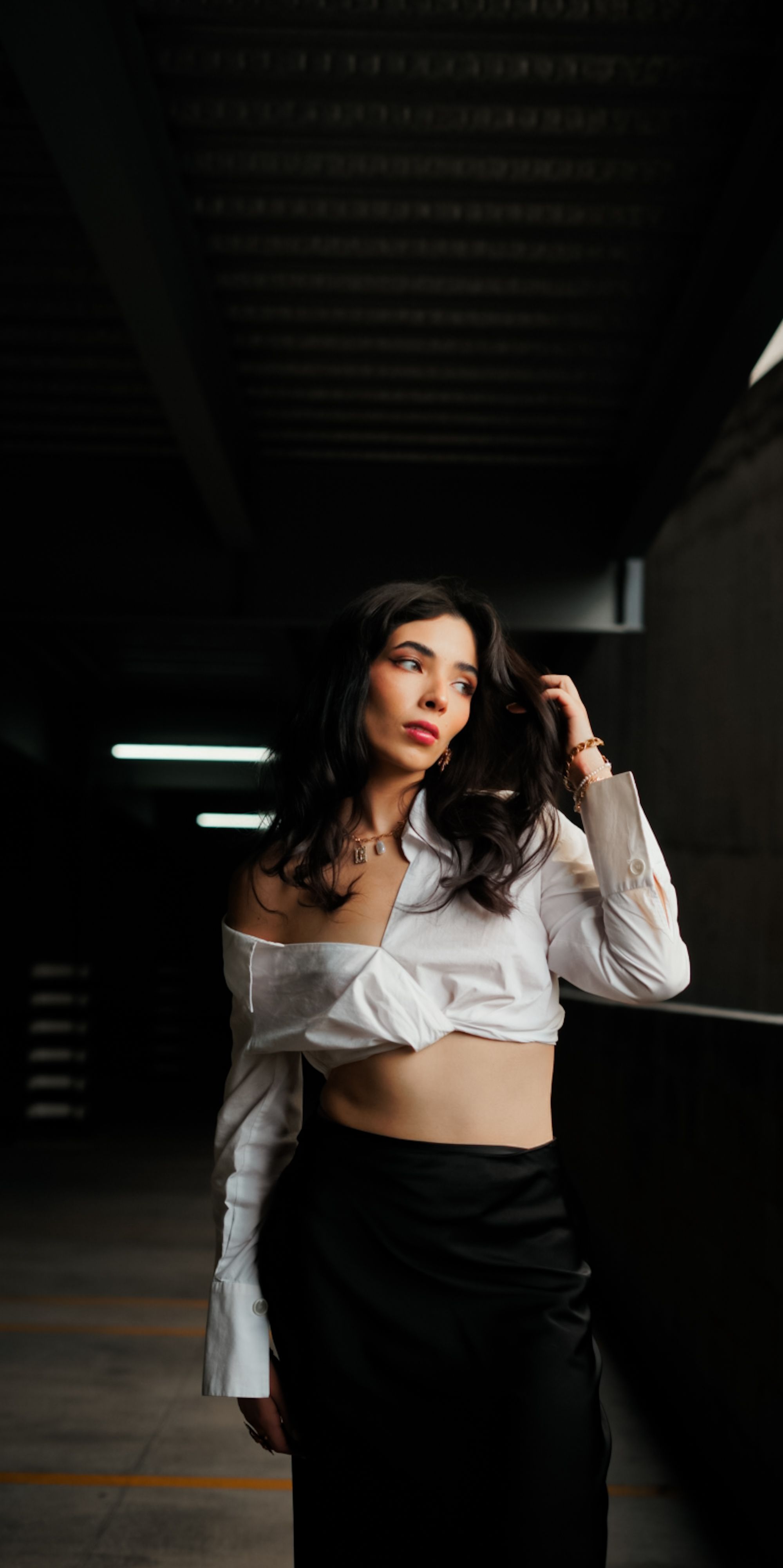 Mulher elegante posa em ambiente urbano com iluminação dramática que realça seu estilo.