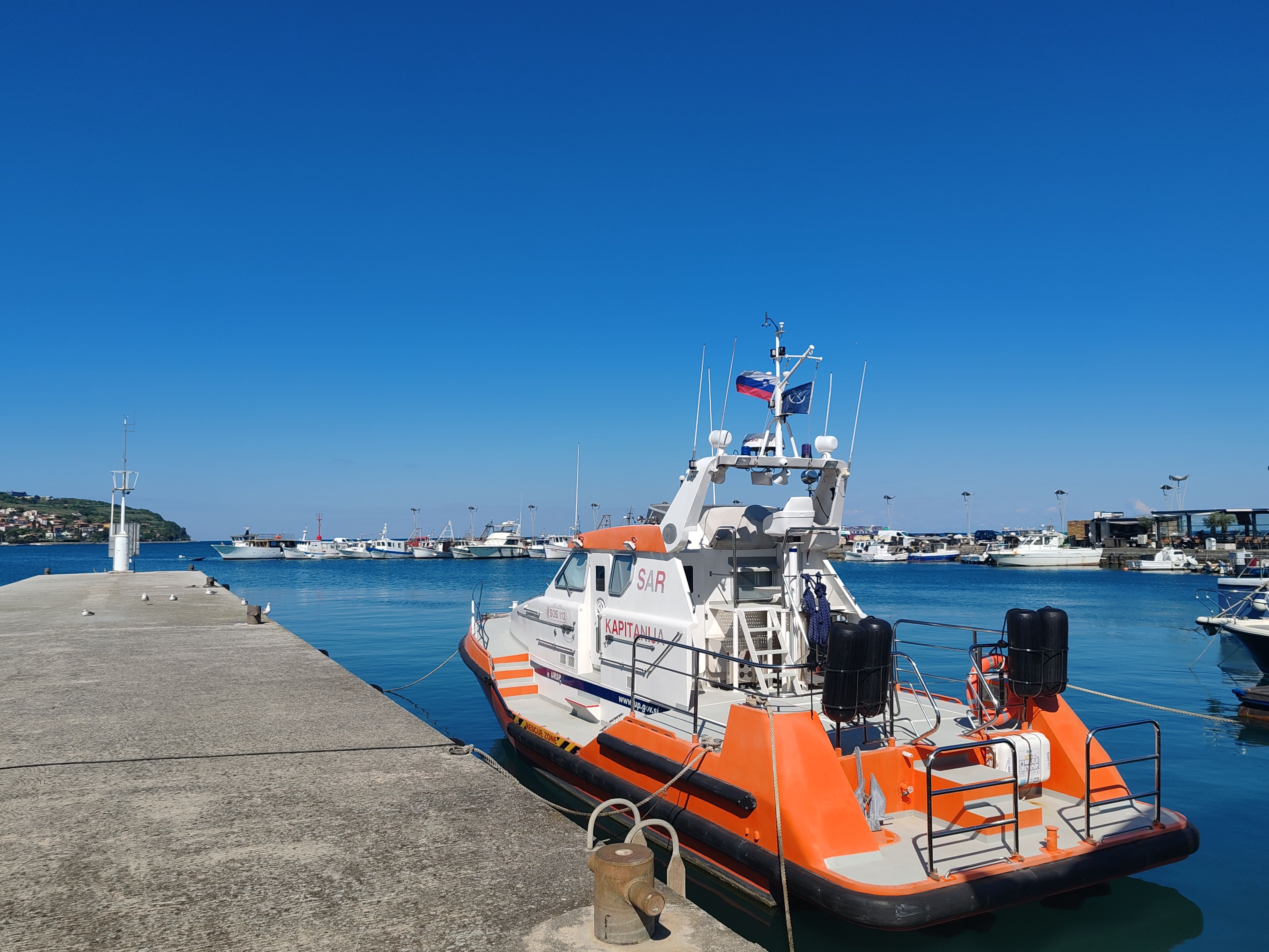 Vibrant rescue boat docked in a scenic marina under clear blue skies.