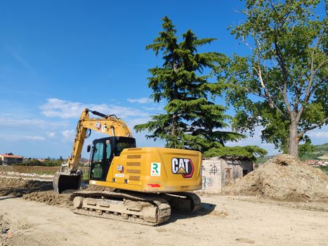 A CAT excavator working at a construction site with trees and blue sky in the background.