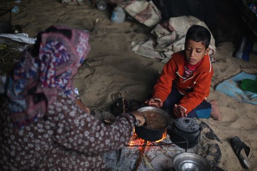 Free A young boy and adult sit by an open fire in a desert camp, cooking a meal together. Stock Photo