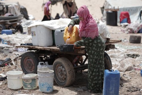 Free A woman fills a container with water at a makeshift camp, highlighting daily survival efforts. Stock Photo