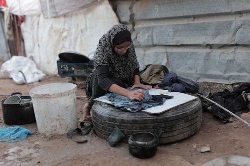 Free Woman handwashing clothes outdoors by a makeshift shelter, showing resilience in challenging conditions. Stock Photo
