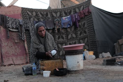 Free A woman in a patterned dress works with household items outdoors near clothes drying on a line. Stock Photo
