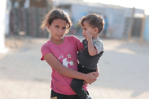 Free A young girl in a pink shirt holds a baby outdoors in a sunny setting. Stock Photo