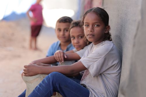 Free Three children sitting by a wall in a relaxed and thoughtful mood outdoors. Stock Photo