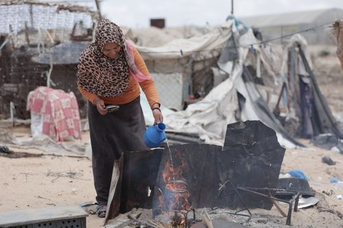 Free A woman using an open fire to prepare a meal in a refugee camp setting. Stock Photo