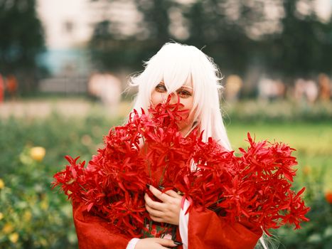 Colorful anime cosplay with red flowers in a Vietnamese garden, showcasing vibrant costumes and floral beauty.