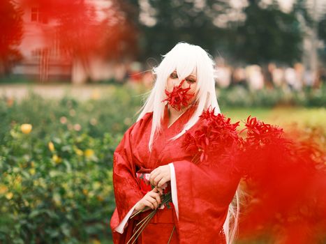 Striking anime cosplay with white hair and red kimono amidst vibrant spider lilies in Vietnam.