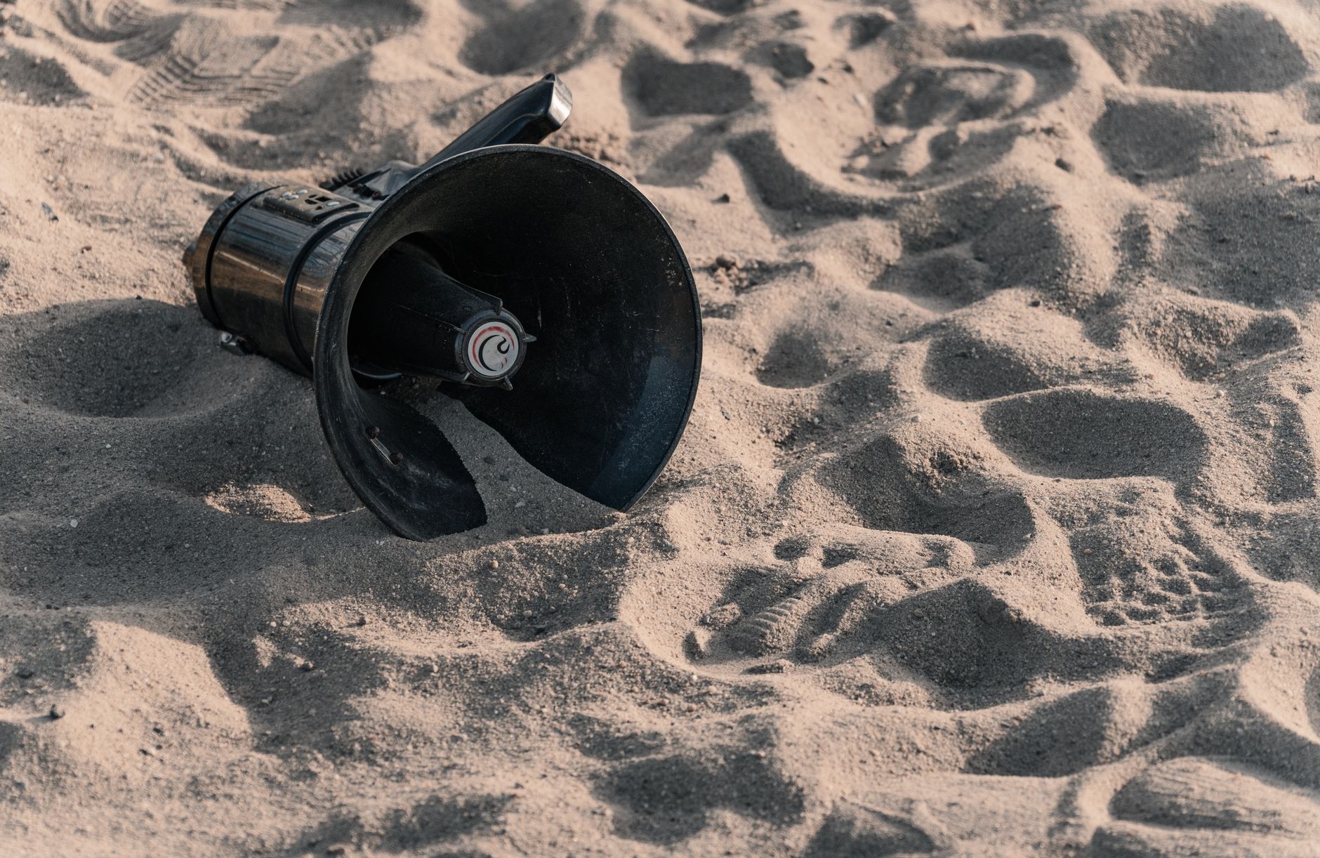 An abandoned black megaphone on sunlit beach sand creates an intriguing contrast.