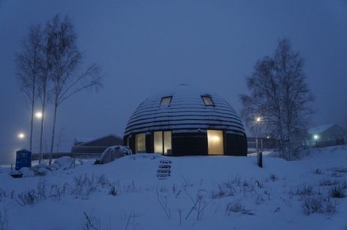 Free A unique dome-shaped building in a snowy, twilight winter setting, with glowing lights inside. Stock Photo