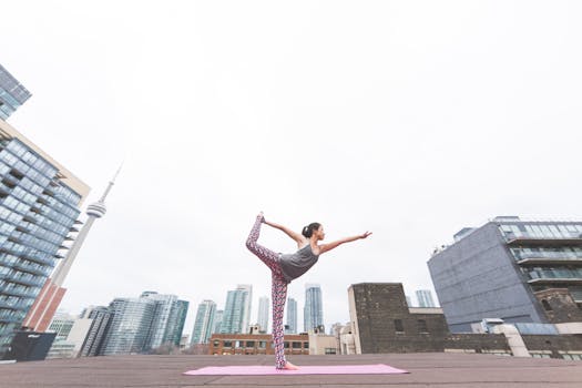 A woman performs yoga on a rooftop overlooking a modern city skyline, embodying balance and urban tranquility.