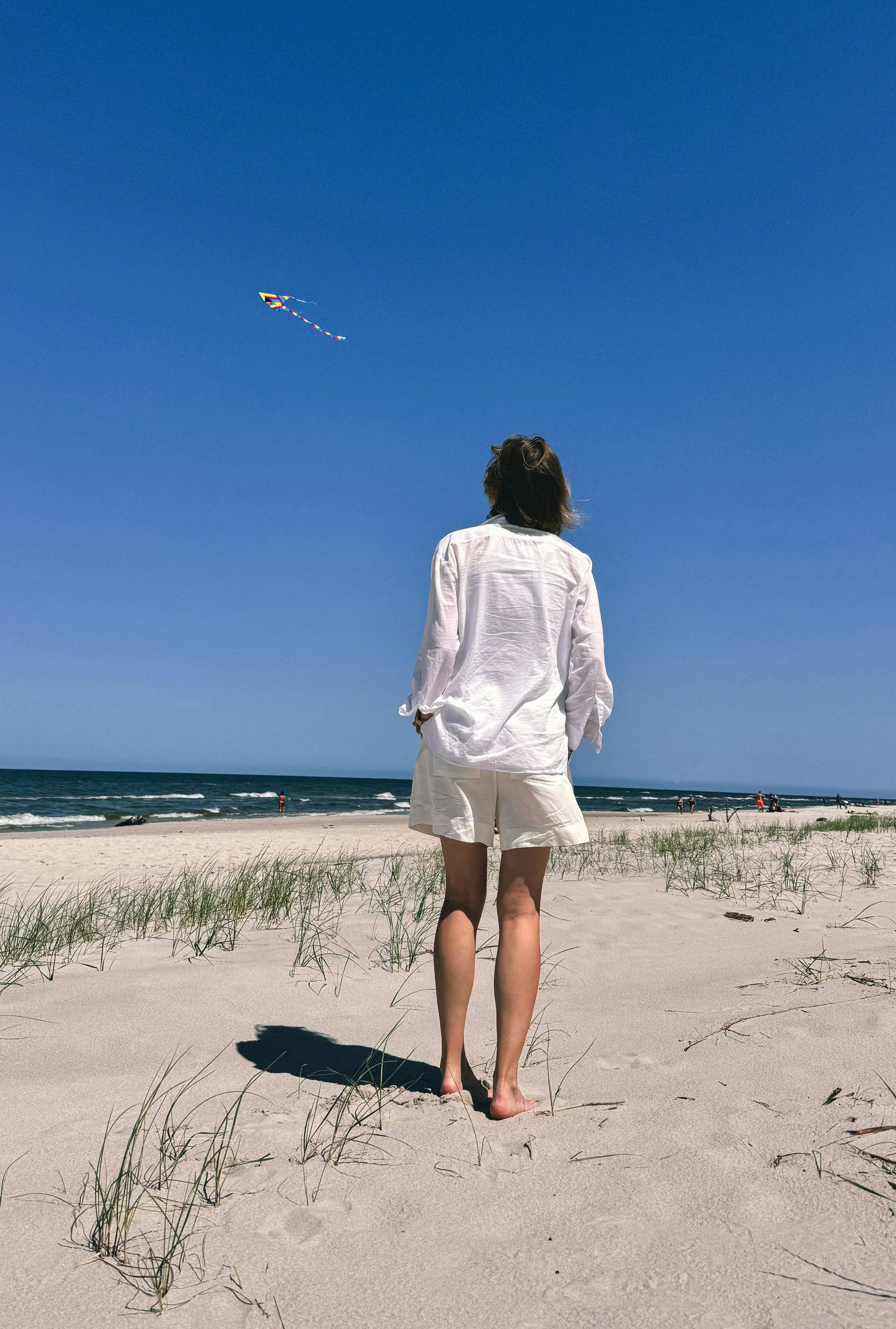 A person enjoys flying a kite on a sunny day by the Baltic Sea coast.