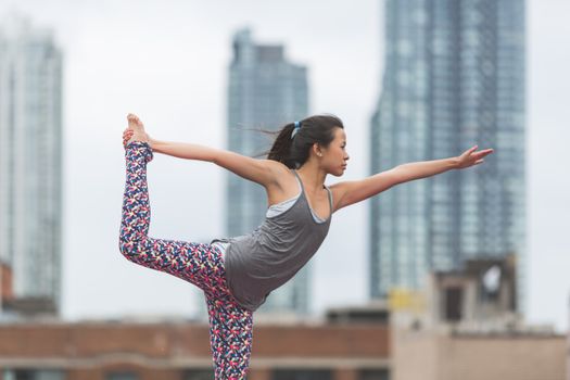 Young woman performing yoga pose outdoors in urban setting with skyscrapers in background.