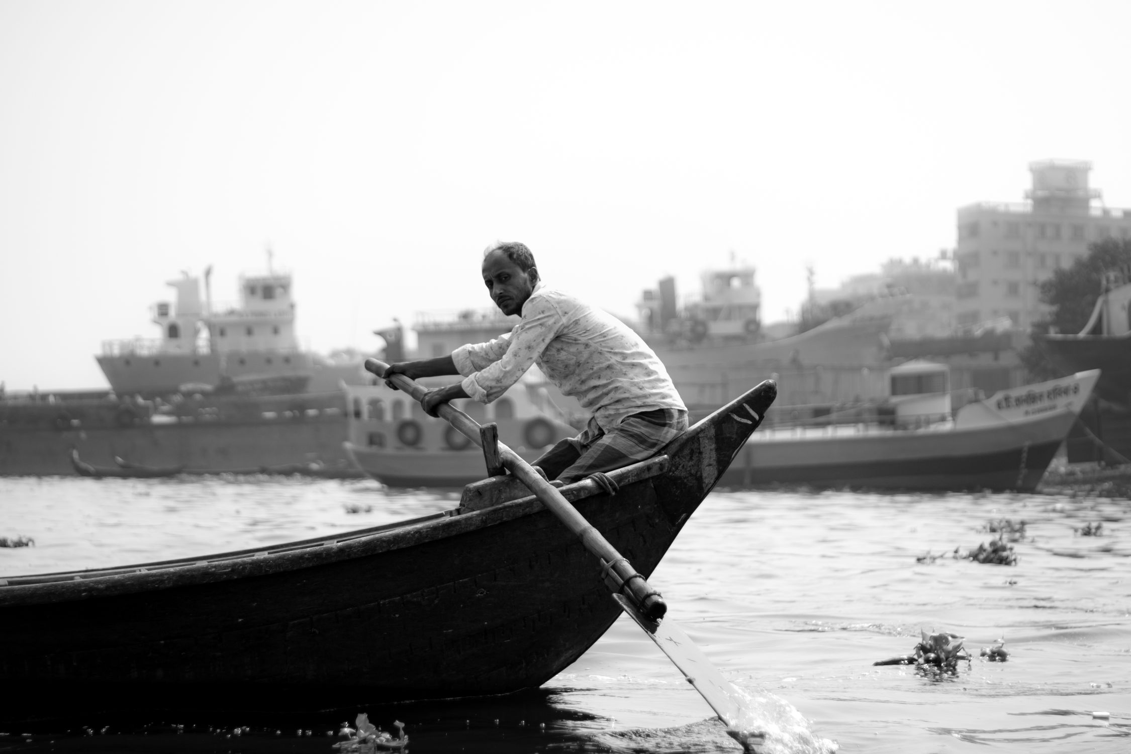 Man Rowing Boat Phot Man rowing a boat on a river with industrial ships · Free Stock Photo