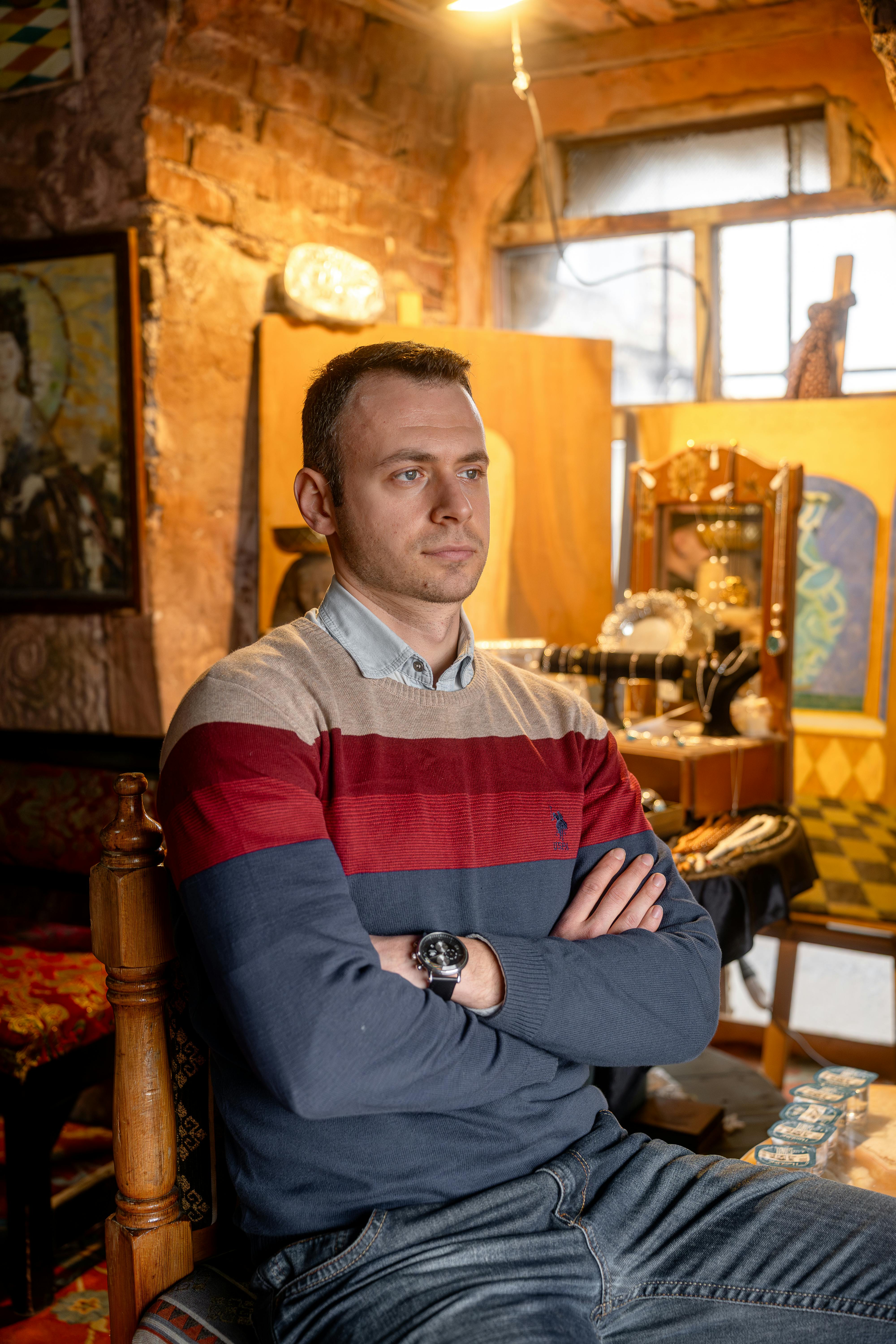 A man sits with arms crossed in a rustic art studio showcasing a comfortable and creative environment.